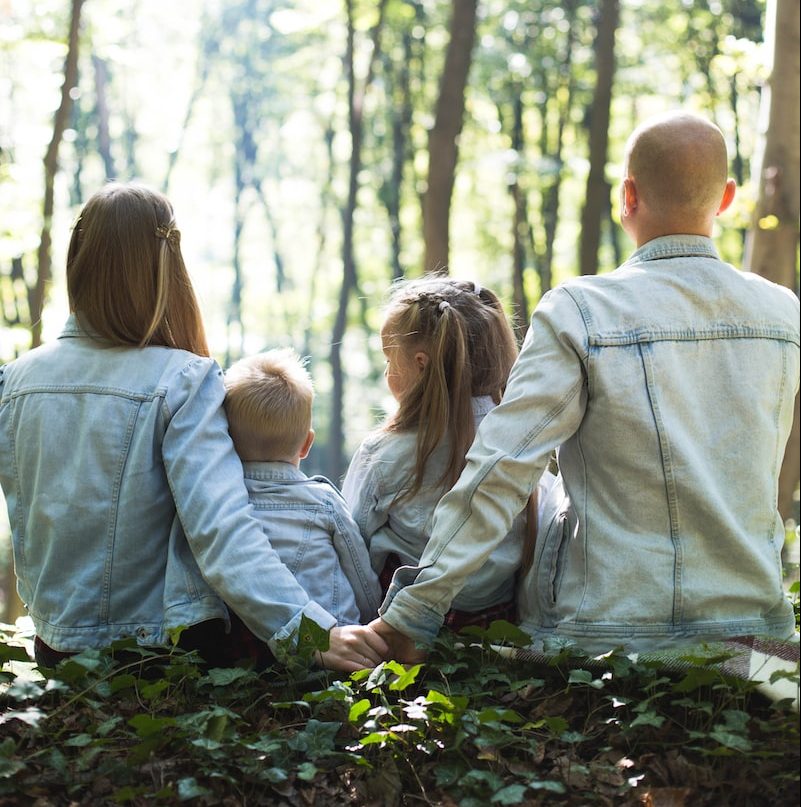 man and woman holding hands together with boy and girl looking at green trees during day